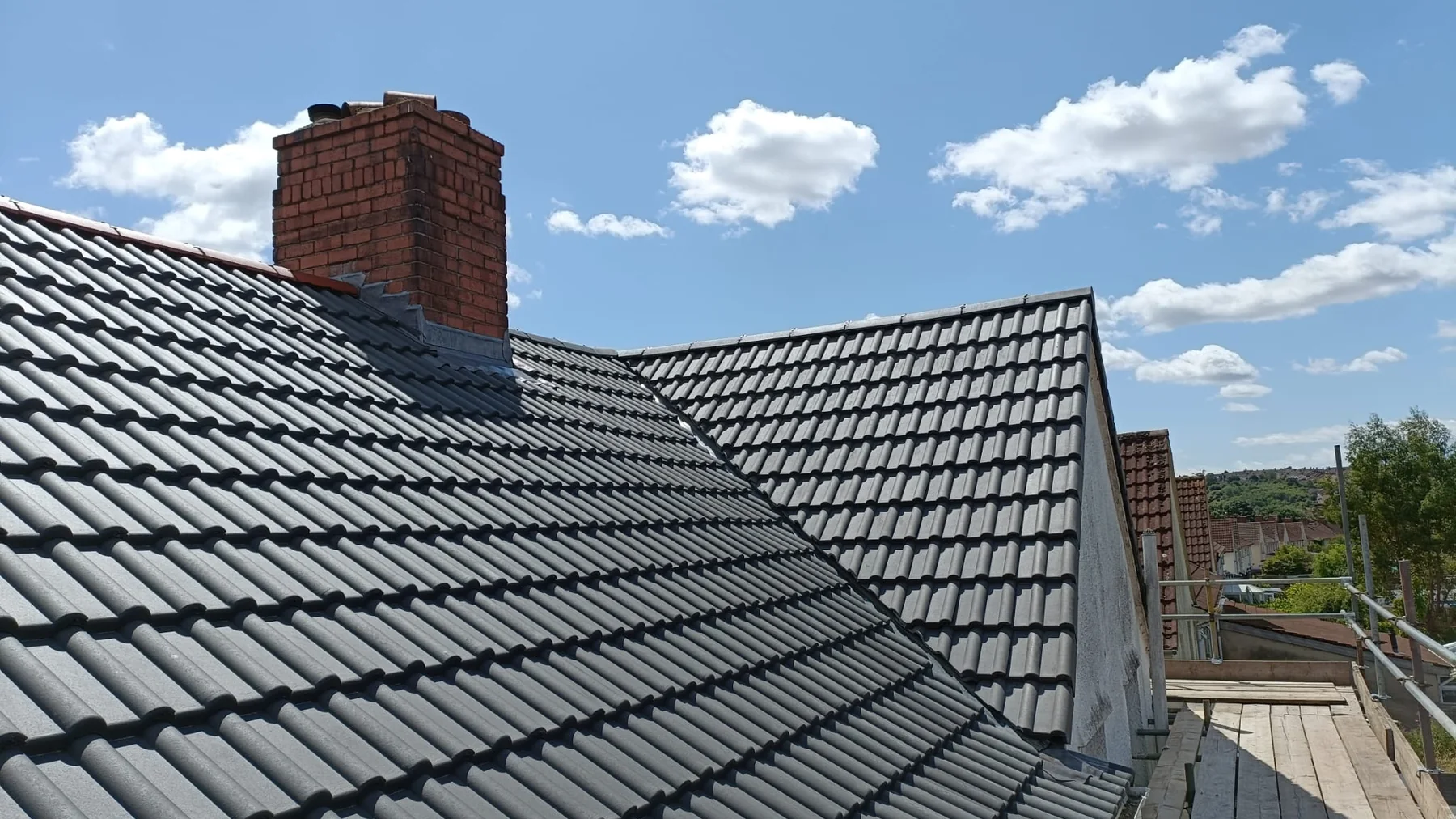 A newly completed dark tiled roof and brick chimney against a blue sky in Bristol
